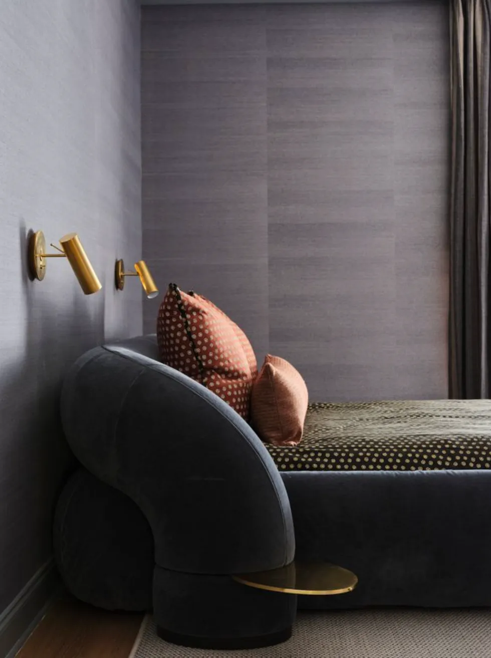 Modern bedroom with curved bed, polka dot pillows and brass wall lights.