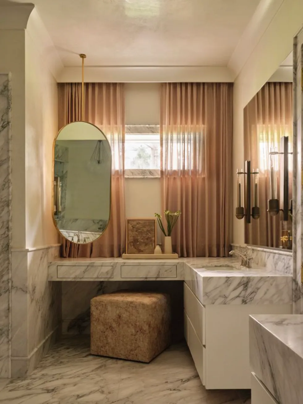 Elegant marble bathroom with oval mirror, vanity, and soft curtains.