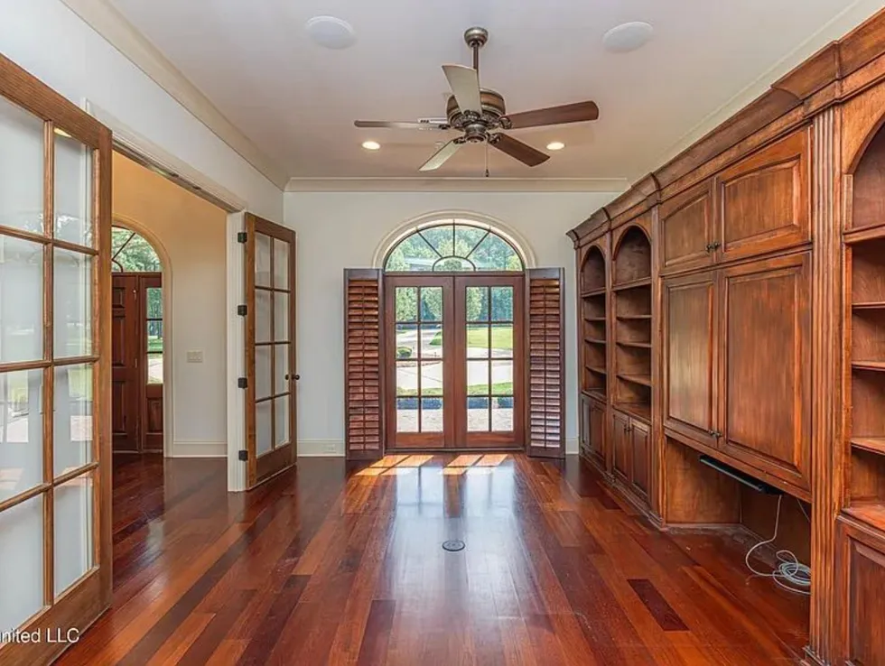 Spacious room with wooden shelves, French doors and a ceiling fan.